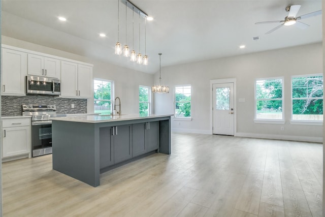 kitchen with decorative backsplash, a kitchen island with sink, ceiling fan with notable chandelier, light countertops, and appliances with stainless steel finishes
