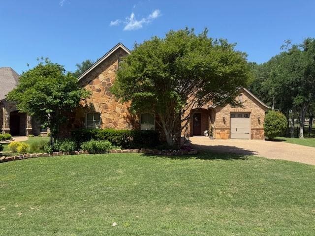 view of front of house with an attached garage, driveway, a front lawn, and stone siding