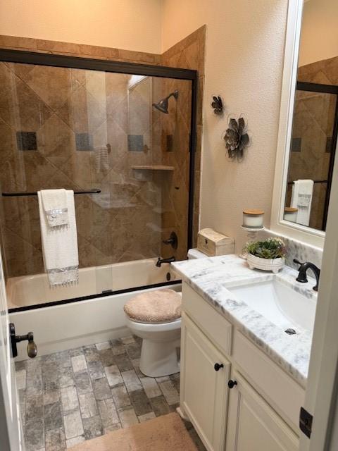 full bath with vanity, combined bath / shower with glass door, and toilet