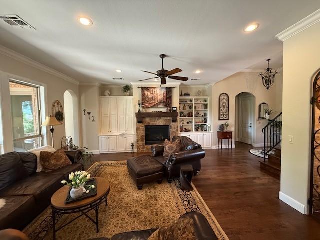 living room with a ceiling fan, visible vents, arched walkways, baseboards, and ornamental molding