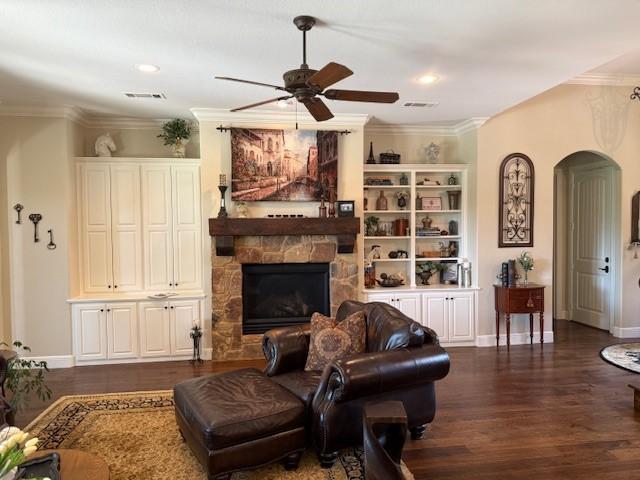 living room with ceiling fan, arched walkways, a stone fireplace, visible vents, and ornamental molding