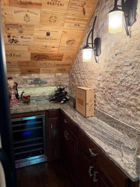 bar with beverage cooler, dark wood-style floors, vaulted ceiling, and a bar