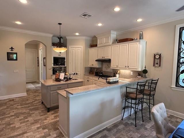 kitchen with visible vents, a peninsula, a kitchen island with sink, under cabinet range hood, and arched walkways