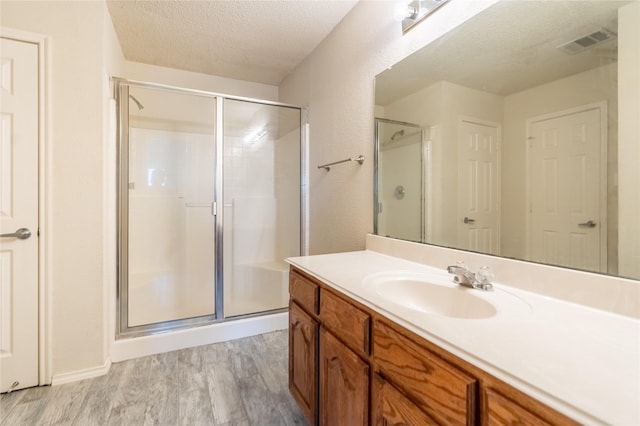 bathroom featuring a textured ceiling, visible vents, a stall shower, wood finished floors, and vanity