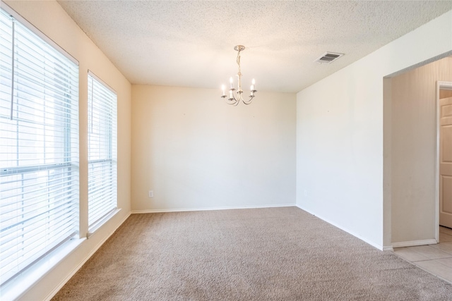 unfurnished room with an inviting chandelier, light carpet, a textured ceiling, baseboards, and visible vents