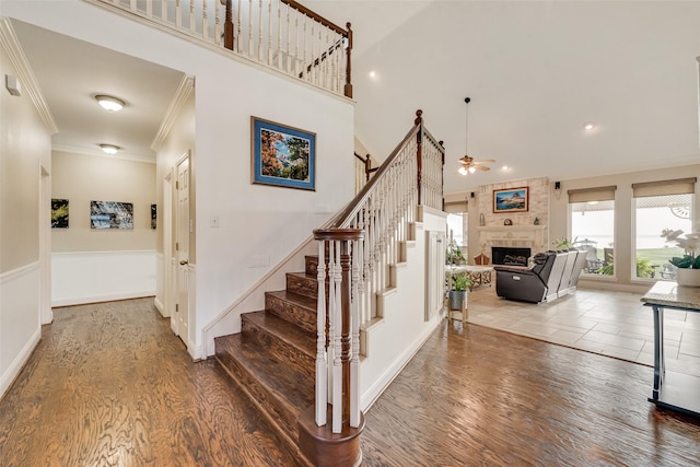 stairs featuring a tile fireplace, a ceiling fan, wood finished floors, a towering ceiling, and ornamental molding