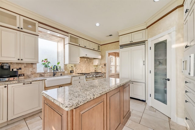 kitchen featuring a sink, light tile patterned floors, under cabinet range hood, visible vents, and paneled fridge