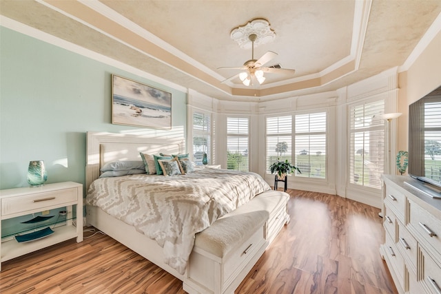 bedroom featuring light wood-style floors, ornamental molding, a raised ceiling, and a ceiling fan