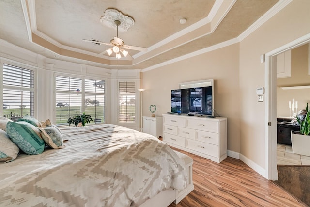 bedroom featuring a ceiling fan, light wood-type flooring, baseboards, ornamental molding, and a tray ceiling