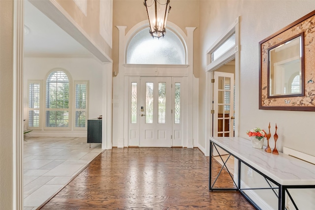 entryway with baseboards, an inviting chandelier, wood finished floors, and a towering ceiling