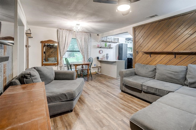 living room with a textured ceiling, wood walls, ceiling fan with notable chandelier, wood finished floors, and visible vents