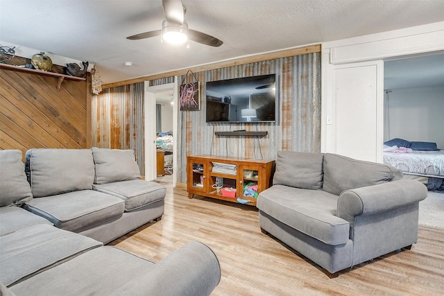 living area featuring a ceiling fan, wood walls, and wood finished floors