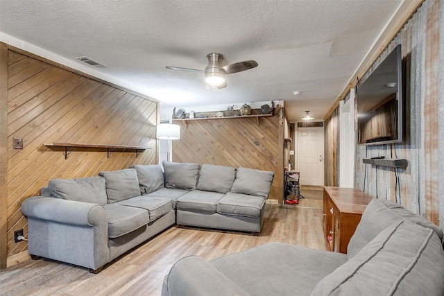 living area with wooden walls, ceiling fan, a textured ceiling, wood finished floors, and visible vents