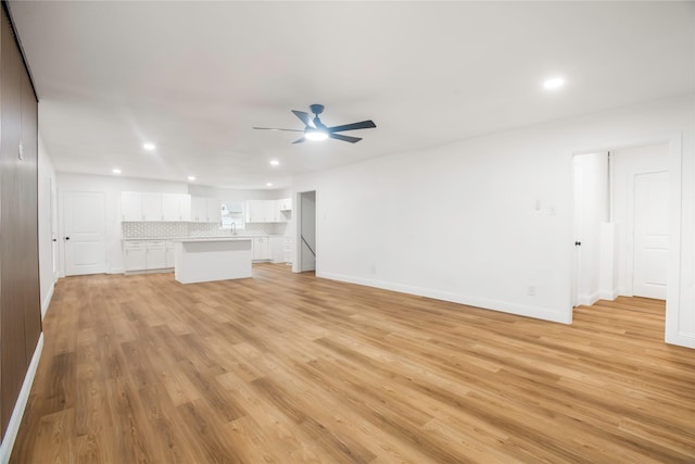 unfurnished living room featuring a ceiling fan, a sink, baseboards, light wood finished floors, and recessed lighting