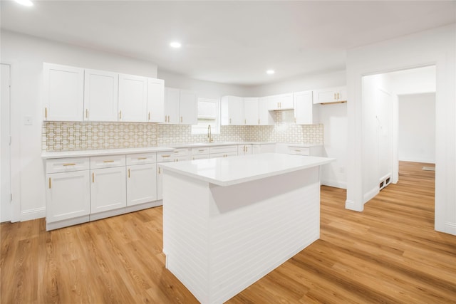 kitchen with white cabinets, a kitchen island, a sink, and light wood-style floors