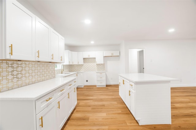 kitchen with white cabinets, a sink, light wood finished floors, a center island, and tasteful backsplash