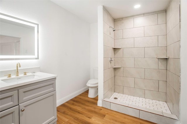 bathroom featuring vanity, wood finished floors, toilet, tiled shower, and recessed lighting