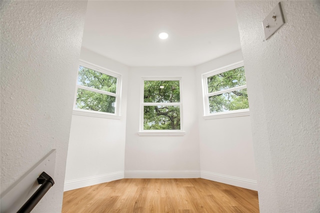 unfurnished room with light wood-style floors, baseboards, plenty of natural light, and a textured wall