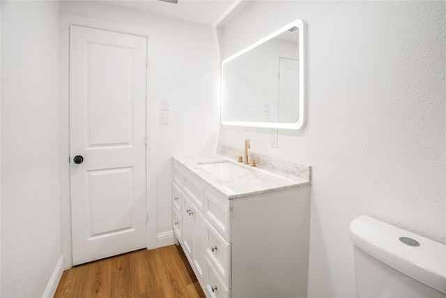 bathroom featuring vanity, baseboards, wood finished floors, and toilet