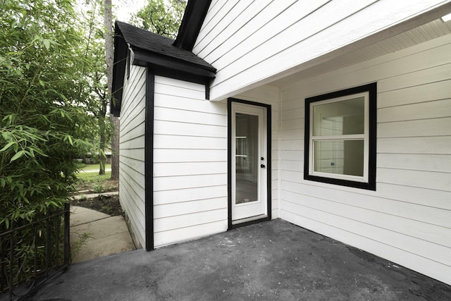 view of exterior entry featuring a shingled roof and a patio area