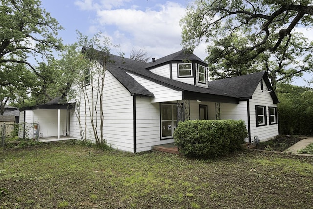 back of house featuring covered porch, a shingled roof, and a yard