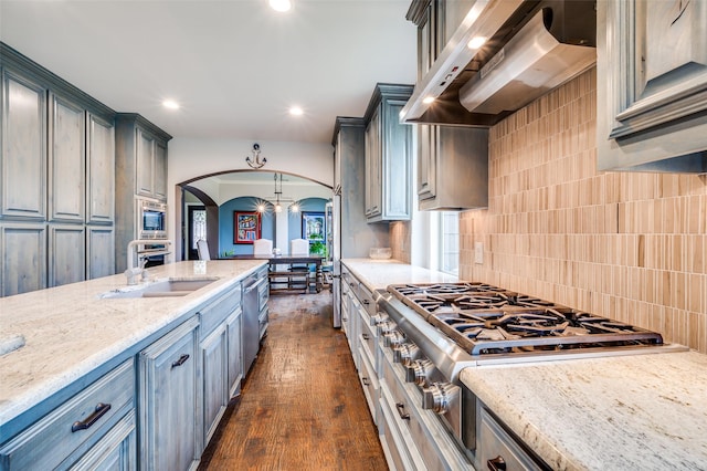 kitchen featuring a sink, wall chimney range hood, tasteful backsplash, arched walkways, and appliances with stainless steel finishes