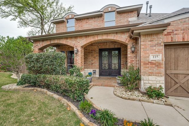 view of exterior entry with covered porch, french doors, brick siding, a shingled roof, and an attached garage