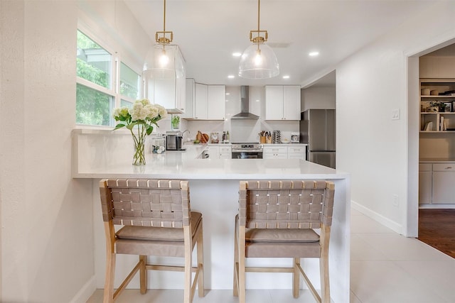 kitchen with white cabinetry, baseboards, freestanding refrigerator, a peninsula, and wall chimney exhaust hood