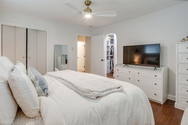 bedroom with a closet, baseboards, ceiling fan, dark wood-style floors, and arched walkways