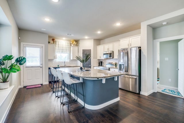 kitchen with white cabinets, dark wood-style flooring, a sink, a kitchen breakfast bar, and stainless steel appliances