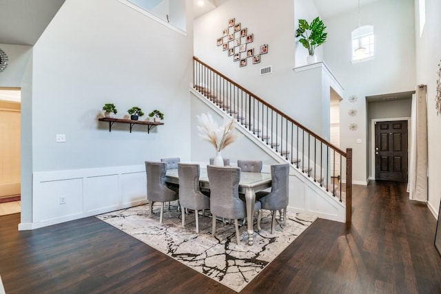 dining room featuring wood finished floors, a high ceiling, visible vents, and stairway