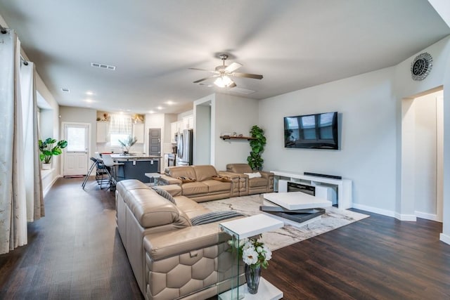 living room featuring visible vents, a ceiling fan, dark wood-style flooring, and baseboards