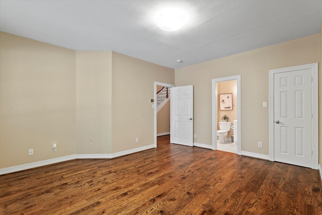 unfurnished bedroom with a walk in closet, baseboards, wood finished floors, and ensuite bathroom