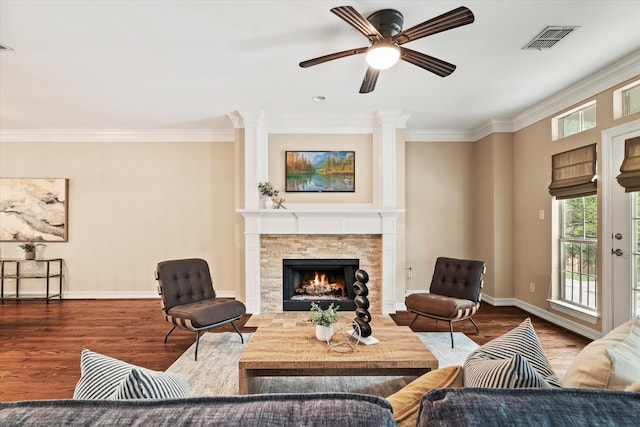 living area featuring a lit fireplace, baseboards, visible vents, and ornamental molding