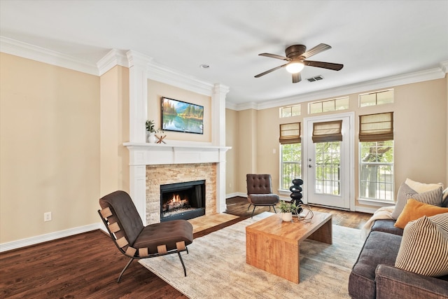 living area featuring ornamental molding, a ceiling fan, a stone fireplace, and wood finished floors