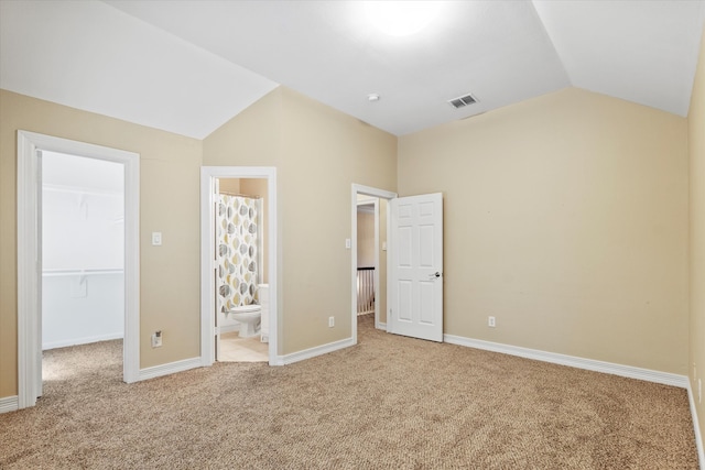 unfurnished bedroom featuring a walk in closet, visible vents, a closet, lofted ceiling, and carpet flooring