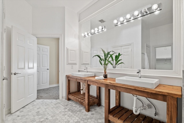 bathroom featuring baseboards, double sink, and visible vents