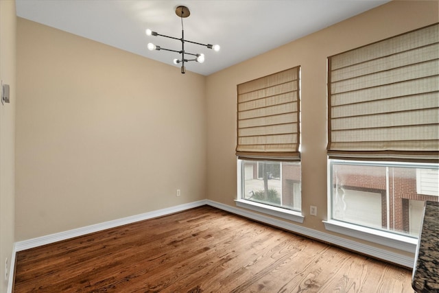 spare room with baseboards, wood finished floors, and a notable chandelier