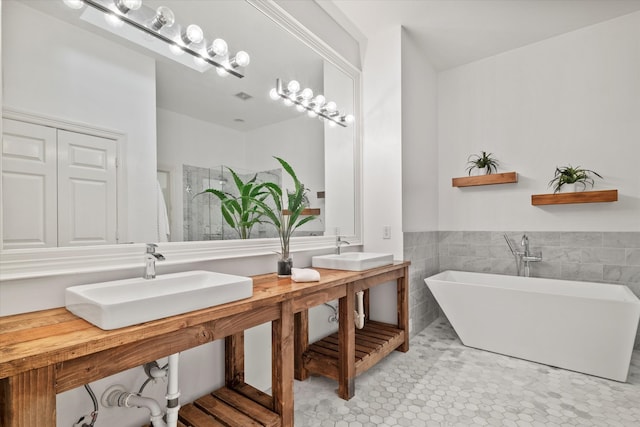 full bathroom with tile patterned flooring, a freestanding tub, tile walls, a wainscoted wall, and double sink