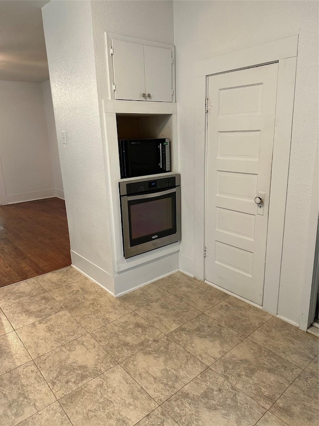 630 W College St, Stephenville, TX 76401 - kitchen featuring stainless steel oven, black microwave, baseboards, and white cabinets
