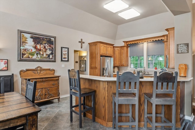 kitchen featuring stainless steel fridge, a sink, light countertops, brown cabinetry, and a peninsula