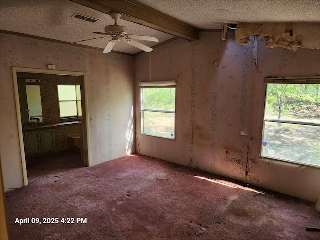 empty room featuring ceiling fan, a textured ceiling, wallpapered walls, vaulted ceiling with beams, and visible vents