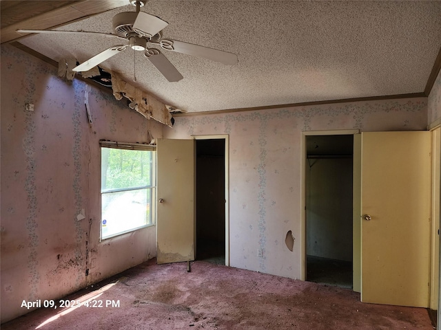 unfurnished bedroom featuring two closets, a ceiling fan, a textured ceiling, and wallpapered walls