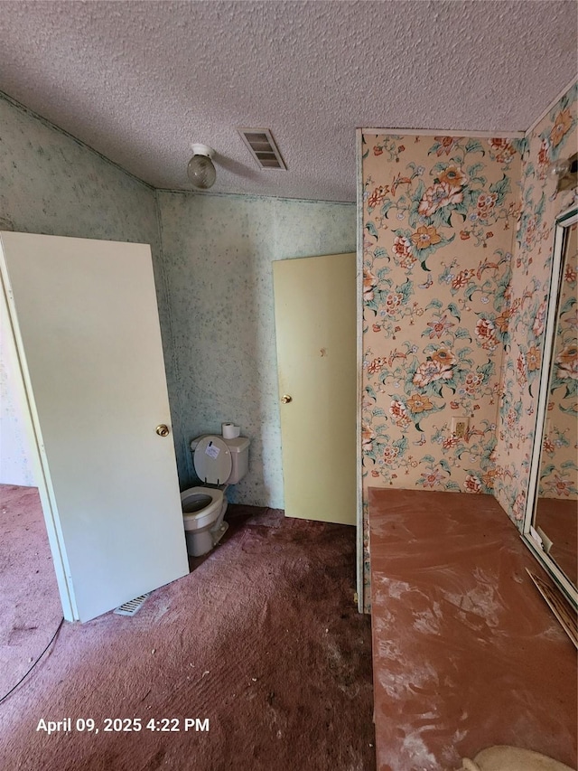bathroom with toilet, wallpapered walls, a textured ceiling, and visible vents