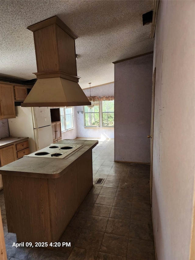 kitchen featuring custom range hood, freestanding refrigerator, a textured ceiling, and cooktop