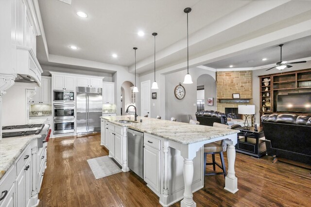 kitchen with ceiling fan, arched walkways, a sink, open floor plan, and built in appliances