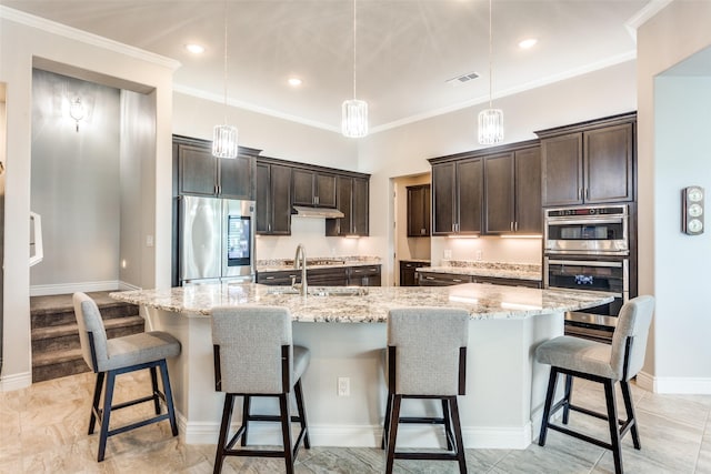kitchen with dark brown cabinetry, appliances with stainless steel finishes, light stone counters, a kitchen bar, and visible vents