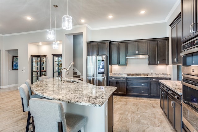 kitchen with dark brown cabinets, appliances with stainless steel finishes, light stone counters, a sink, and a kitchen bar