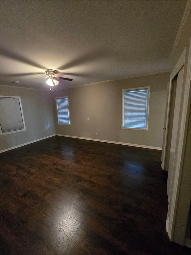 spare room featuring baseboards, ceiling fan, dark wood-style flooring, and a textured ceiling