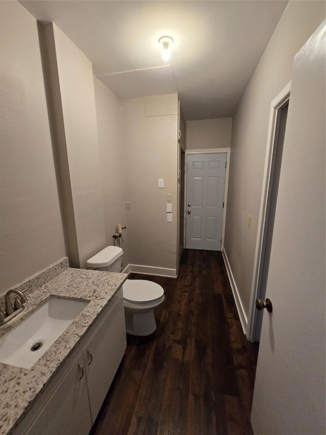 half bath featuring vanity, baseboards, toilet, and wood finished floors